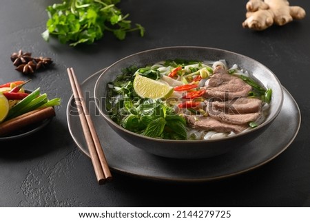 Pho Bo traditional Soup with beef, rice noodles, ginger, lime, chili pepper in bowl. Close up. Vietnamese and Asian cuisine.