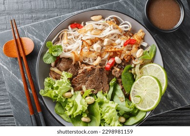 Pho Bo Tron Mixed beef noodles salad is a popular dish in Vietnamese cuisine closeup on the bowl on a wooden table. Horizontal top view from above