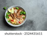 Pho Bo Vietnamese soup, bowl of fresh asian soup with rice noodle, beef, herbs, soy sprouts and chili on concrete background, top view, copy space. Delicious asian food.