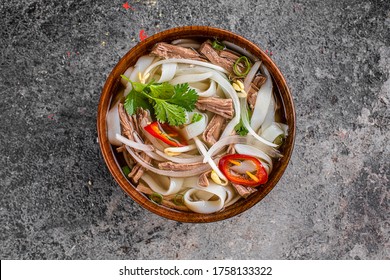 Pho Broth, Vietnamese Soup In A Deep Plate With Meat, Wooden Chinese Sticks And Two Quail Eggs On A Dark Background