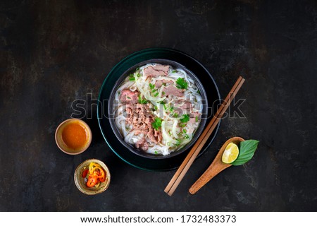 Pho Vietnam on the dark kitchen table. Beef noodle or Pho Bo is beef, rice noodle, herb in delicious broth. Serving with chili, chili sauce, lime. Best street food of Vietnam