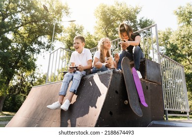 Phone Addicted Sports Children With Skateboard And Penny Boards Smiling And Looking At Smartphones On Sports Ramp On Playground. Kids Addiction Of Phones