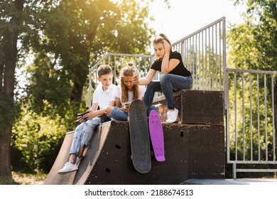 Phone Addicted Sports Children With Skateboard And Penny Boards Are Sitting And Looking At Smartphones On Sports Ramp On Playground. Kids Addiction Of Phones