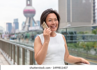 Phone Asian woman mature middle age chinese businesswoman talking business on mobile smartphone call outside on Shanghai street with Pearl tower in background. China travel.
