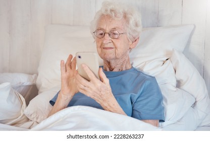 Phone, bed and senior woman in nursing home surfing internet, social media or nostalgic photographs with happy memories. Communication, technology and grandma in bedroom of retirement home with smile - Powered by Shutterstock