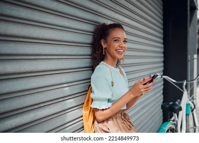 Phone, bike and black woman on wall in city, street or urban outdoors. Travel, bicycle and happy student from Nigeria on 5g mobile tech, social media or internet surfing, web browsing or text message - Powered by Shutterstock