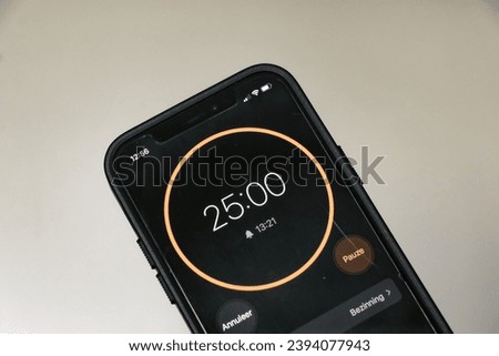 A phone with a black and orange 25-minute timer to study with the pomodoro method on a blurry background. Translation: Pauze means Pause in Dutch. 