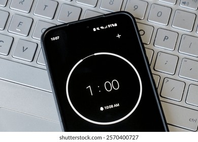 A phone with a black and white 1-minute timer to study with pomodoro method on laptop keyboard, study business background