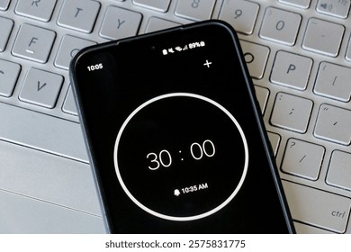 A phone with a black and white 30-minute timer to study with pomodoro method on laptop keyboard, study office business background