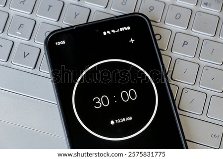 A phone with a black and white 30-minute timer to study with pomodoro method on laptop keyboard, study office business background