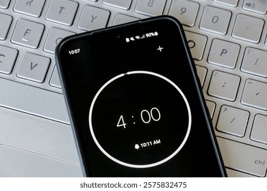 A phone with a black and white 4-minute timer. Mobile phone laying on laptop keyboard, study, homework, learning, office, business background