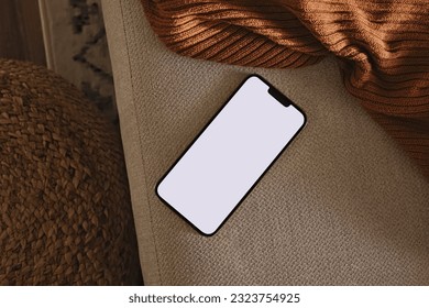 Phone with blank screen lying on the sofa with brown plaid. Modern minimal still life, smart phone mock-up - Powered by Shutterstock