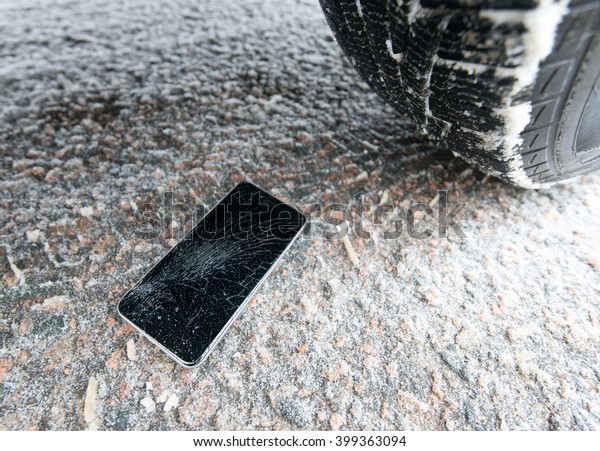 Phone with broken\
screen on snow in car trail. Glass covered with snow flakes. Device\
run over by wheel.