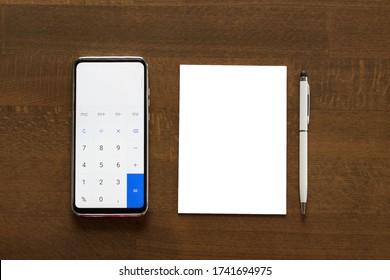 A Phone Calculator, A Blank Paper And A Pen On Wooden Background.