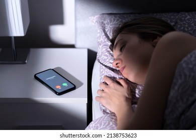 Phone call by unknown caller at night while woman is sleeping in bed. Scam, fraud or mobile hoax from suspicious fake number. Illegal mobile crime. Tired person asleep. Stalker or stranger bullying.