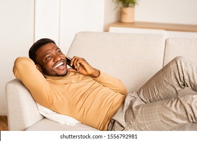 Phone Call. Happy Afro Man Talking On Cellphone Lying On Couch At Home.