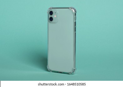 Phone Case Mock Up Side View. Mint Green IPhone 11 In Clear Silicone Case Isolated On Green Background, Rotated Position. Smartphone Perspective View