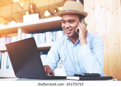 phone to colleague. Confident young asian man in smart casual wear holding smart phone and looking at outside while sitting at his working place in office.