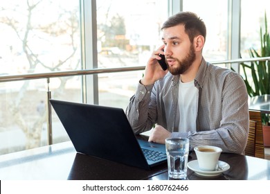 Phone conversation. Upset young man talking over phone disappointed hear bad news. Portrait tired, exhausted man in cafe or modern office with smartphone and laptop. Attractive businessman freelancer - Shutterstock ID 1680762466