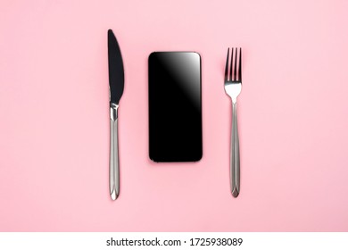 Phone with copy space for text and a fork with a knife on a pink background