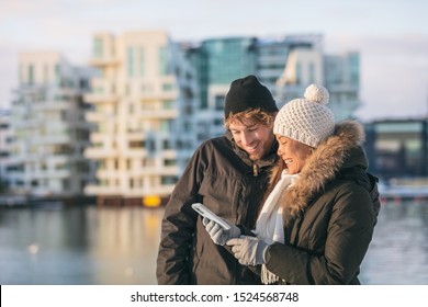 Phone Couple Using Mobile On Winter City Walk Walking Outside On Street Looking Up Directions On Online App. Happy Asian Woman And Caucasian Man.