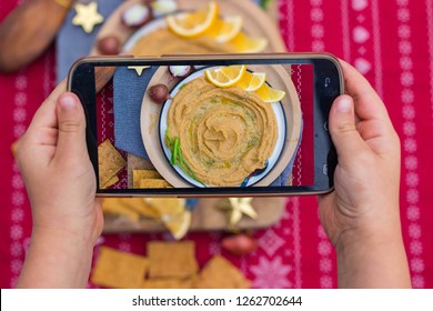 Phone Food Photo. Kids Hands Take Smartphone Food Photography Of Israeli Arabic Hummus Chickpea Dip Spread On Plate For Social Networks Or Blogging. Vegan, Vegetarian Healthy Food 