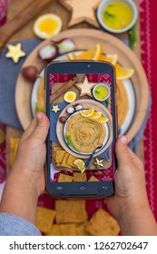 Phone Food Photo. Kids Hands Take Smartphone Food Photography Of Israeli Arabic Hummus Chickpea Dip Spread On Plate For Social Networks Or Blogging. Vegan, Vegetarian Healthy Food 