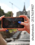 A phone in the foreground captures the Hercules Fountain in Kassel, its screen displaying the majestic statue and cascading water. The iconic monument rises proudly in the background.