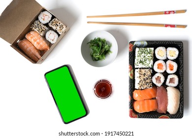 Phone With Green Screen On A White Table With Sushi Food In Take-away Containers. Mock Up Mobile. Take-away Food, Online Shopping Concept.