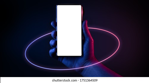 Phone In Hand. Silhouette Of Male Hand Holding Bezel-less Smartphone With Futuristic Neon Light Circle On Dark Background. Screen Is Cut With Clipping Path.