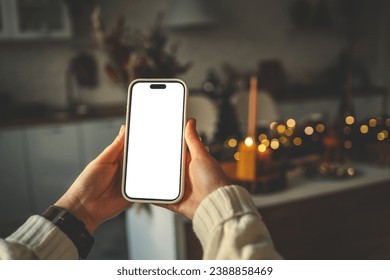 Phone in hands with isolated screen on Christmas kitchen background.