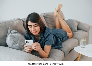 With Phone. Laying Down On The Sofa. Young Woman Is At Home. Conception Of Beauty.