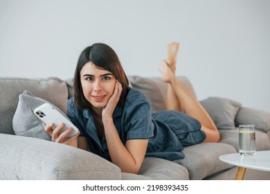 With Phone. Laying Down On The Sofa. Young Woman Is At Home. Conception Of Beauty.