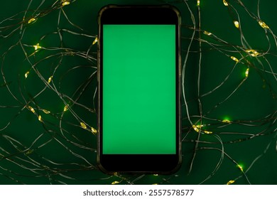 The phone lies horizontally with a green chromakey screen against a garland of yellow and green lights on a green background. High quality photo