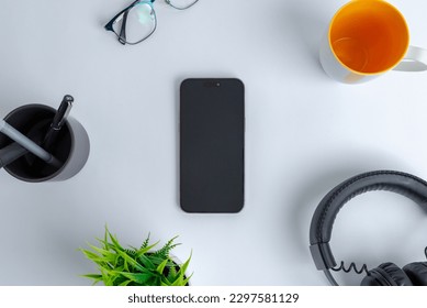 Phone on work desk. Top view, flat lay composition. Surrounded by coffee mug, headset, plant, glasses and pens - Powered by Shutterstock