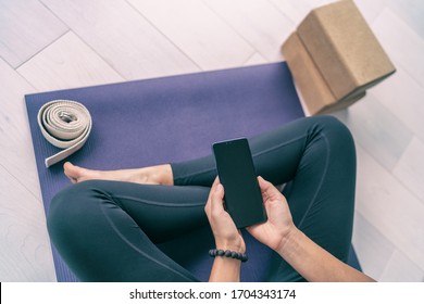 Phone online fitness class fit woman using mobile app at home for strength training workout videos in apartment looking at cellphone screen. Top view of exercise mat.