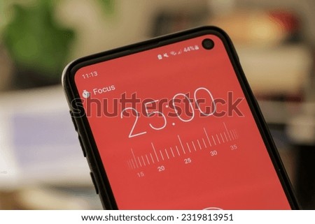 A phone with a red 25-minute timer to study with the pomodoro method on a blurry background. Perfect for students planning their time studying, doing homework, being productive.