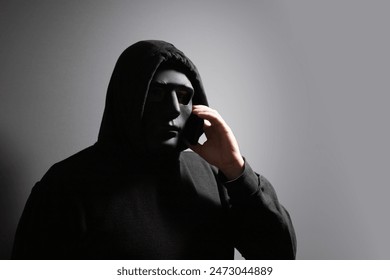 Phone Scammers, man in a mask with a phone, criminal network stealing data, hacker breaking into accounts, online safety compromised. - Powered by Shutterstock