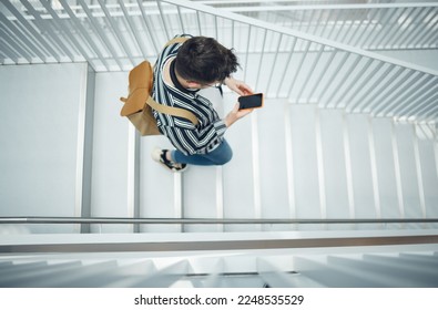 Phone, stairs and education with a student man walking down a staircase at university or college. Mobile, study and top view with a male pupil taking steps to get to class for learning or development - Powered by Shutterstock