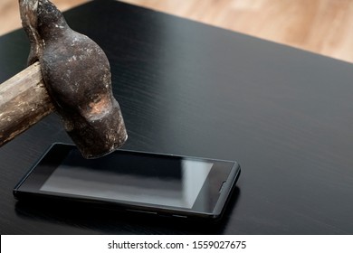 Phone Under Hammer Isolated On Wooden Table