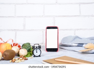 Phone With White Mockup, Little Clock, And Different Kitchen And Cooking Utensils On Light Table. Culinary Blog, Recipe Template, Online Cooking Courses. Healthy Food Concept