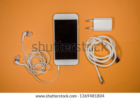 a phone with white usb cable, block and headphones on orange background. Keep the battery charged and listen to music on your device anyway you go. Tehnology connect close up.