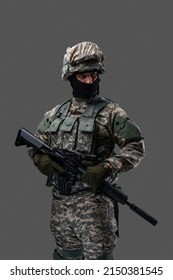 Phot of brave serviceman dressed in vest and uniform holding rifle against gray background.