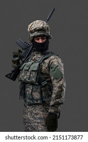 Phot of brave serviceman dressed in vest and uniform holding rifle against gray background.