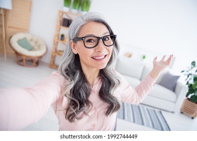 Phot of cheerful elderly woman happy positive smile make selfie show hands empty space demonstrate home