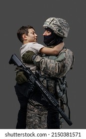 Phot of proud military man with rifle embracing young boy isolated on gray background.
