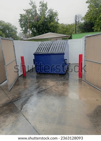 Photo of an 8 yard blue front load dumpster inside an enclosure. 