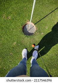 Photo From Above Of Womans Legs On Green Grass With Golf Ball And Golf Cue Before  Hole