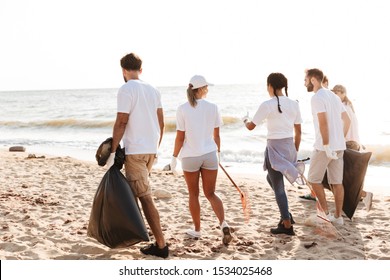 Photo of active eco volunteers people cleaning beach from plastic with trash bags at seaside - Powered by Shutterstock