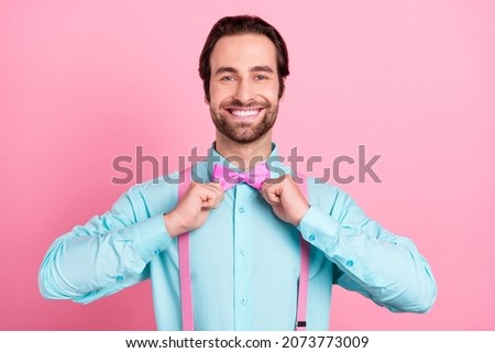 Photo of adorable charming young guy dressed teal clothes adjusting bowtie smiling isolated pink color background